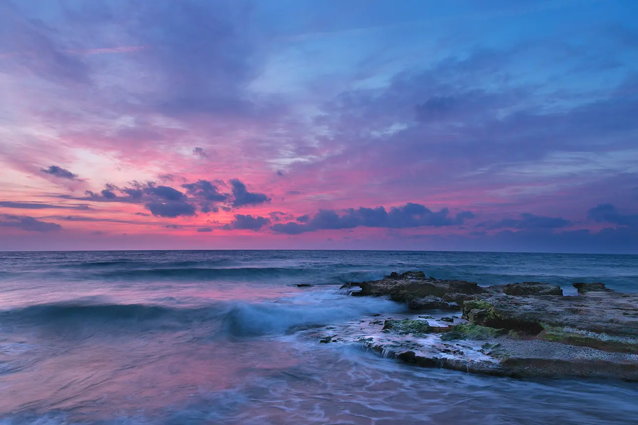 purple and pink sunset over the ocean and some algae covered rocks